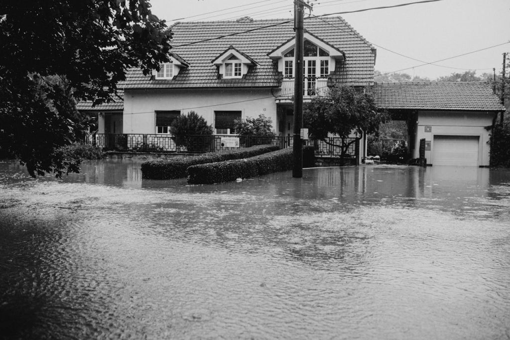 black-and-white-photo-of-flooded-suburban-house-28447778 A black and white image showing a suburban house surrounded by floodwater.