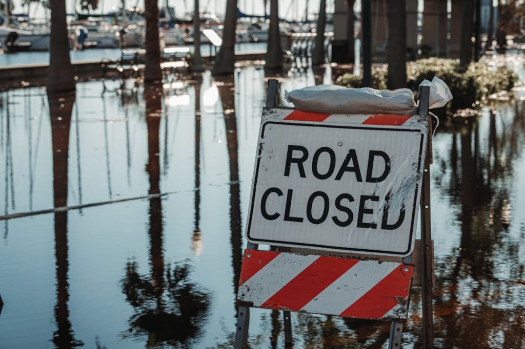 road-closed-signage-on-street-13865778 Road closed sign amidst flooded street, reflecting calm water and trees.